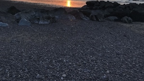 A pebbled beach with a sunset over the water, rocky outcrops, and distant mountains. - Cedar House (Minehead)