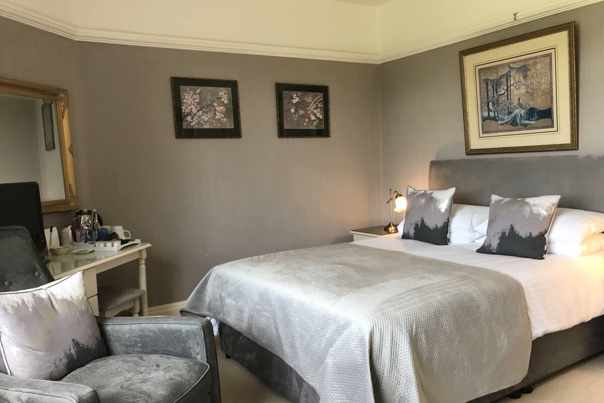 Une chambre d’hôtel avec un grand lit, un bureau avec une chaise, une table de chevet et deux œuvres d’art encadrées accrochées au mur.