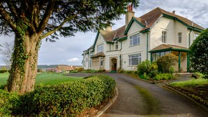 A large, two-story house with a traditional design, featuring a prominent front entrance and a well-maintained garden. - Cedar House (Minehead)