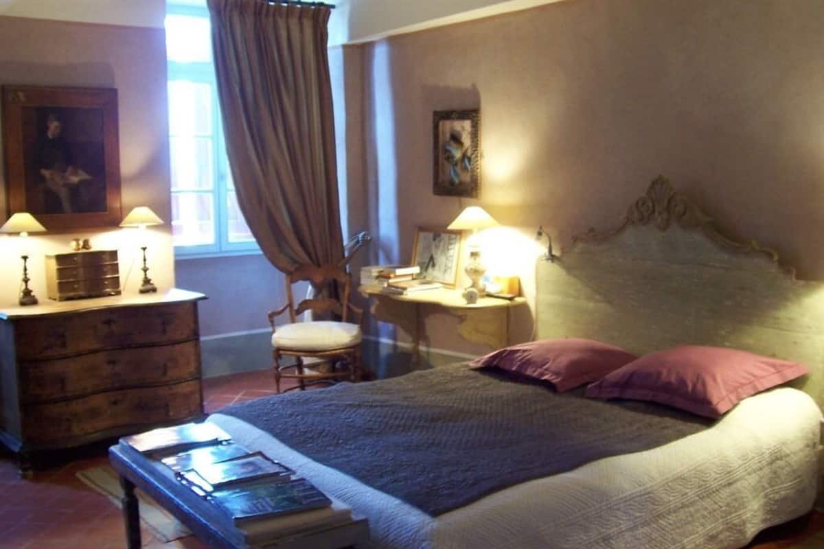 Un dormitorio con cama, mesita de noche, lámpara, silla y cómoda.