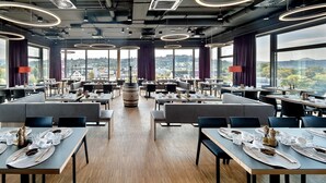 A modern restaurant with multiple dining areas, large windows offering scenic views, and contemporary lighting fixtures. - Hotel am Remspark (Schwaebisch Gmuend)