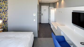 A hotel room with a bed, a TV, a desk, and a blue chair.