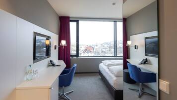 Habitación de hotel con cama, dos sillas azules, escritorio, televisor y ventana con vista a la ciudad.