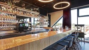 A modern bar with a wooden counter, shelves of liquor bottles, and a coffee machine. - Hotel am Remspark (Schwaebisch Gmuend)