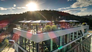 A rooftop terrace with outdoor seating and a view of a forested hill. - Hotel am Remspark (Schwaebisch Gmuend)