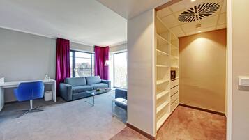 Un soggiorno moderno con divano, tavolino e scrivania con sedia. È presente una grande finestra con tende e un lampadario decorativo al soffitto.