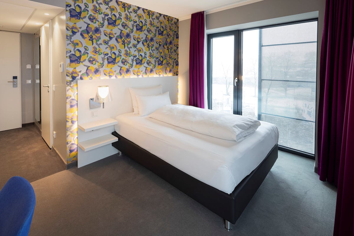Ett modernt hotellrum med en stor säng, en rymlig klädkammare, ett badrum och utsikt genom ett stort fönster.