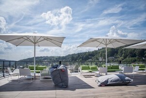 Una terraza en la azotea con sombrillas blancas, sillones reclinables blancos y verdes, y un asiento informal tipo bean bag gris.
