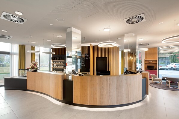 Una moderna zona de recepción con un mostrador curvo de madera, iluminación colgante y vistas a la calle.