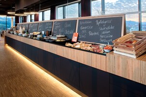Un mostrador de buffet con diversos alimentos y un menú en pizarra que enumera platos como 'Quark' y 'Käsespickel'.