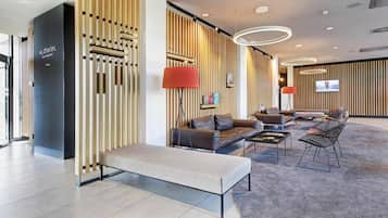 A modern lobby with a reception desk, seating area, and a TV screen.