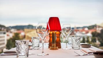 Een tafel gedekt met wijnglazen en een rode lamp, met uitzicht op een stadsbeeld.