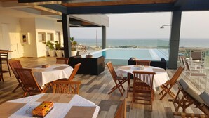 A rooftop terrace with wooden tables and chairs, a pool, and a view of the sea. - Suncity Apartments Hotel (Accra)