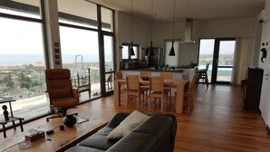 A spacious living area with a large sofa, a dining table, and a kitchen in the background. - Suncity Apartments Hotel (Accra)