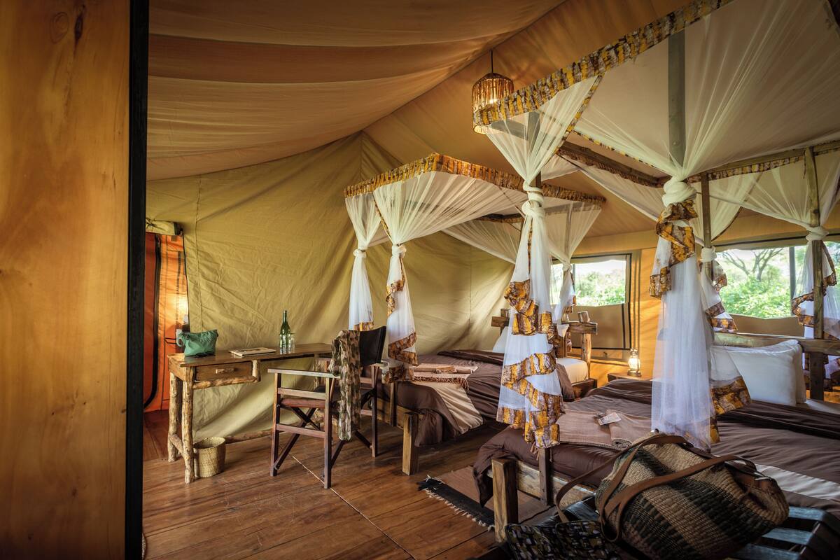 A tented room with four beds, each with a canopy, a wooden table, and a chair.