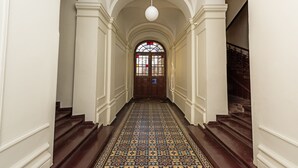 A hallway with a patterned floor, white walls, and a wooden door with a stained glass window. - Magic Apartments (Kraków)