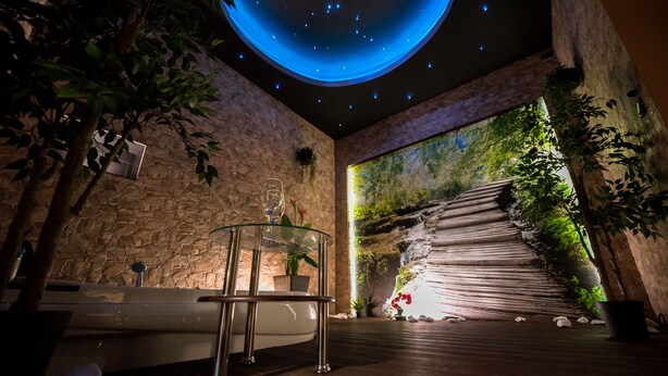 A modern spa area with a stone wall, a glass table with a glass, and a large mural of a forest scene. - Magic Apartments (Kraków)