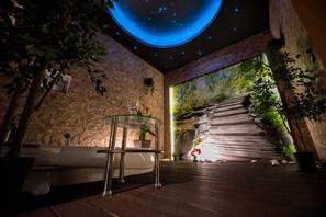 A modern spa area with a stone wall, a glass table with a glass, and a large mural of a forest scene. - Magic Apartments (Kraków)