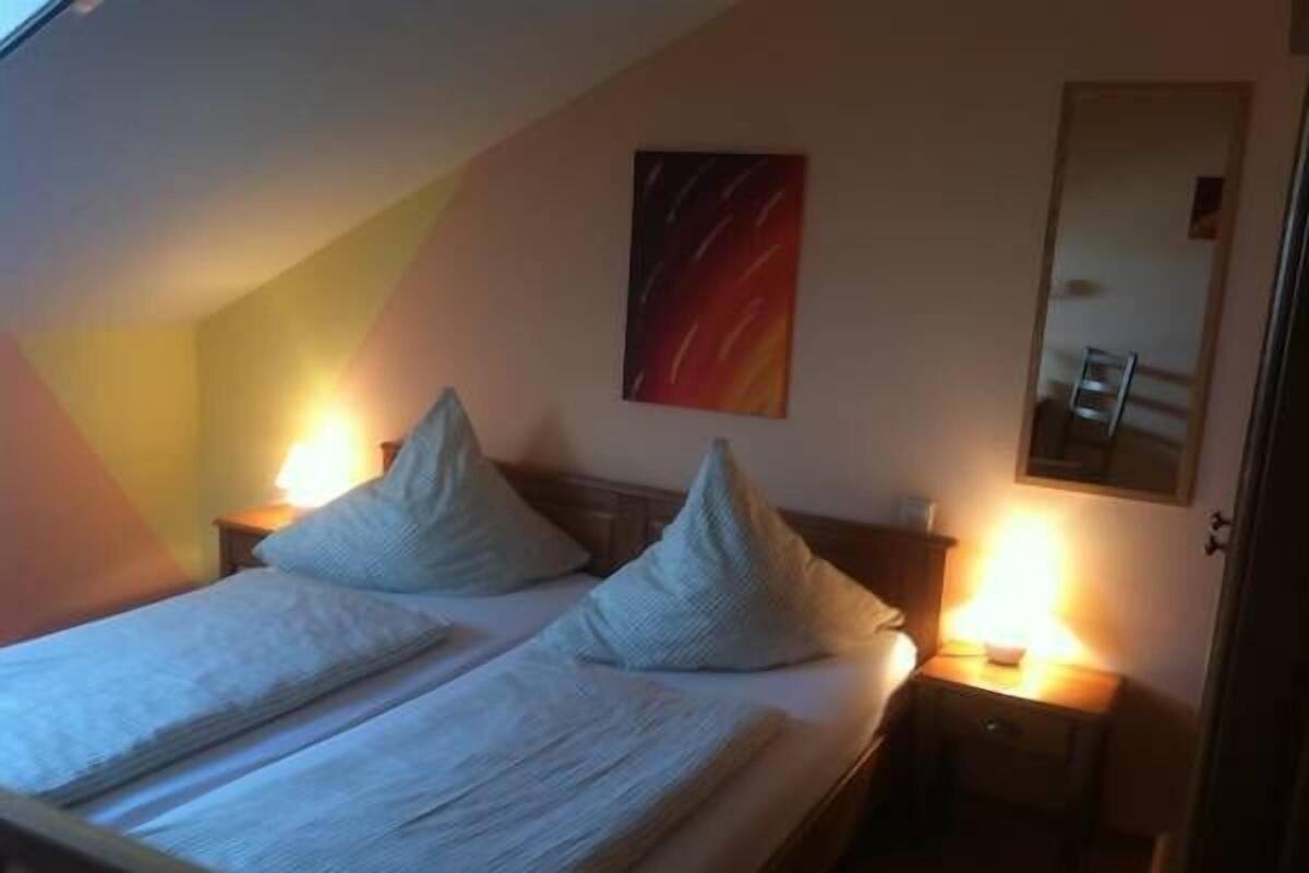 A bedroom with a bed, two bedside lamps, a nightstand, a mirror, and a painting on the wall.