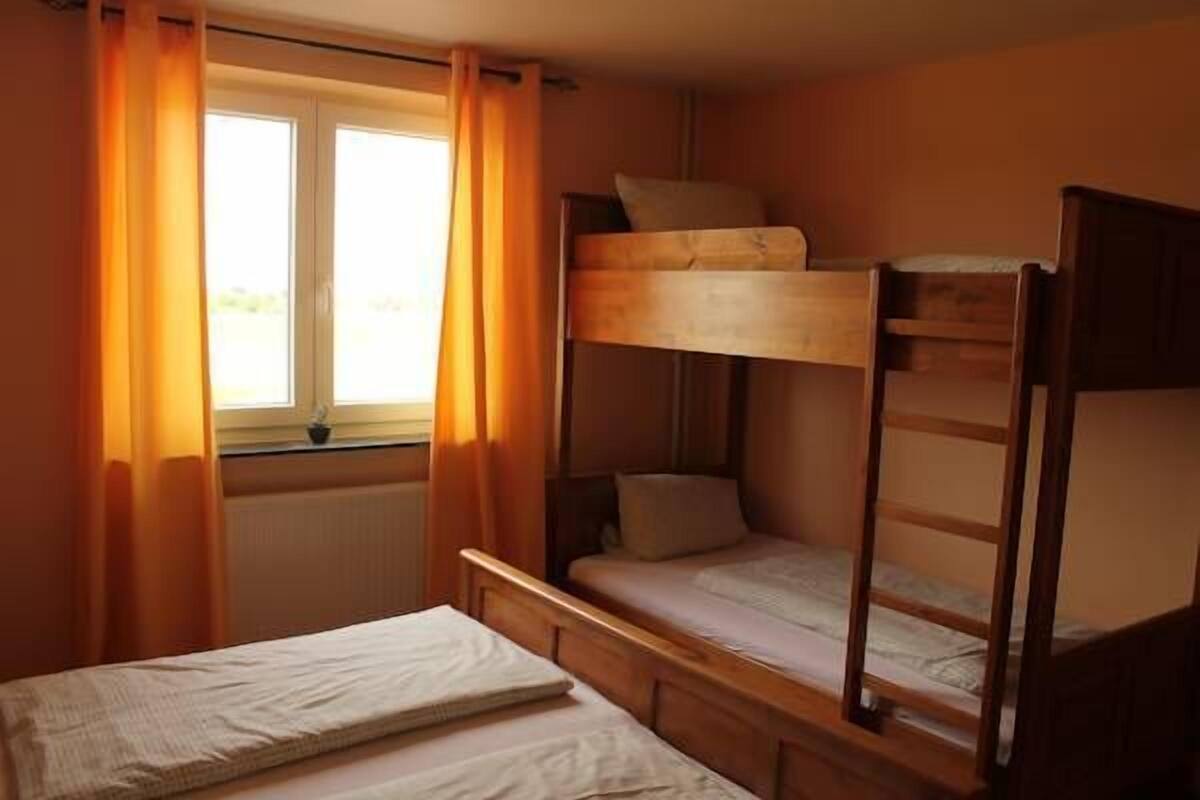 A room with a bunk bed, a single bed, and a window with curtains.