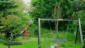 A playground with a swing set and a slide in a lush green area. - Pension A'MiRo (Rust)