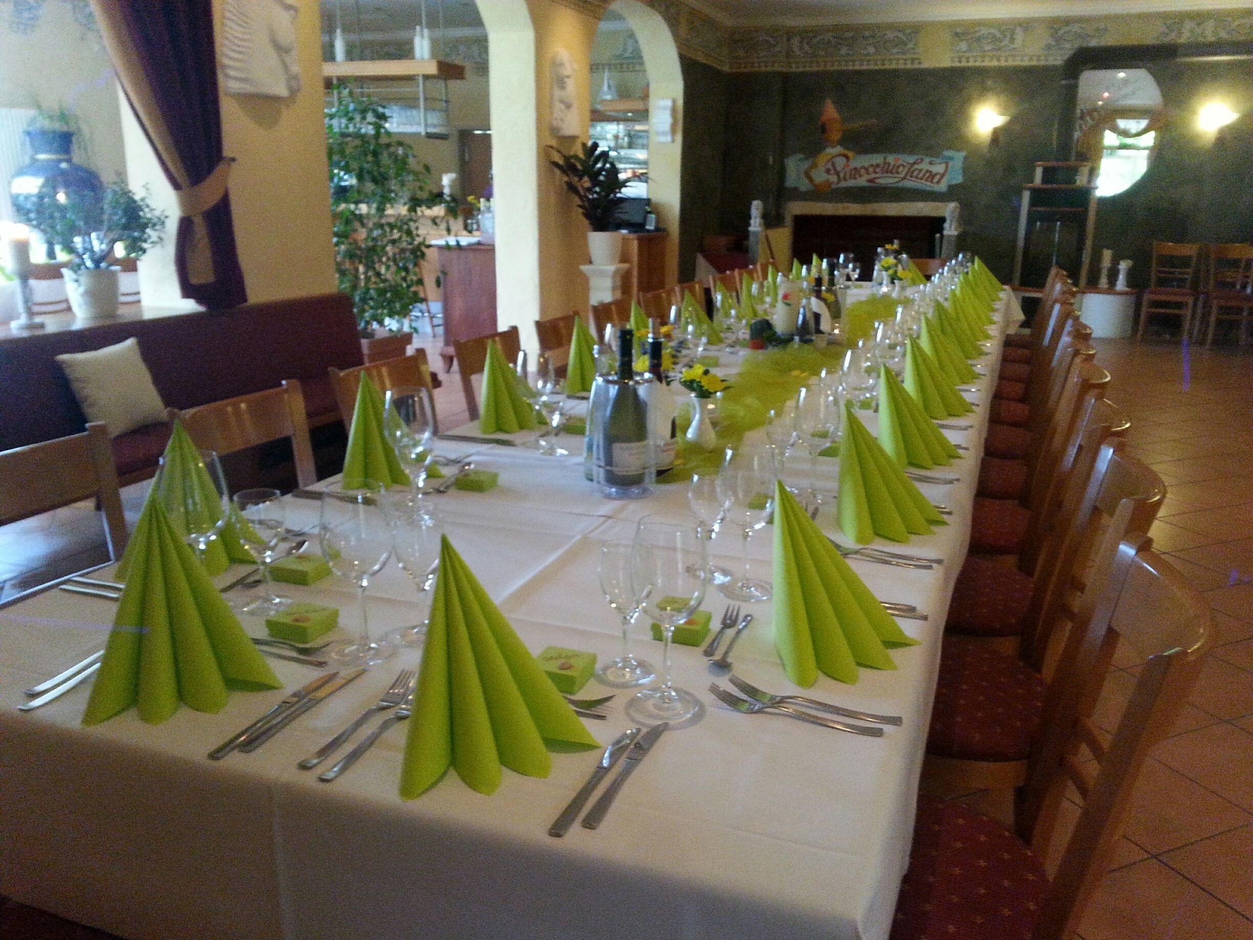A long dining table set with green napkins, silverware, and wine glasses, with chairs aligned on both sides.