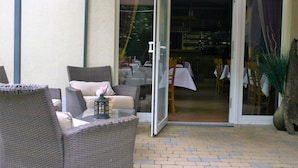 An outdoor seating area with wicker furniture and a glass door leading to an indoor dining space. - Pension A'MiRo (Rust)