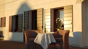 Un espace extérieur aménagé avec deux fauteuils confortables et une table, le tout installé devant un bâtiment aux volets en bois et au sol carrelé.