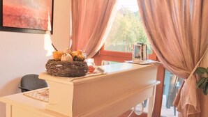 Un coin repas avec une table blanche, un panier de fruits et un tableau accroché au mur.