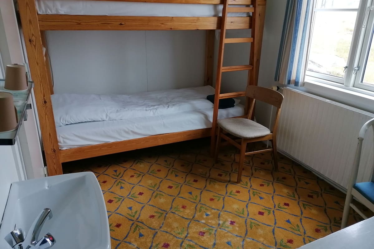 A bunk bed room with a wooden ladder, a chair, a sink, and a window with curtains.