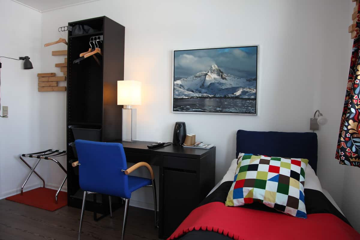 A bedroom with a bed, a desk, a chair, a wardrobe, a lamp, and a picture on the wall.
