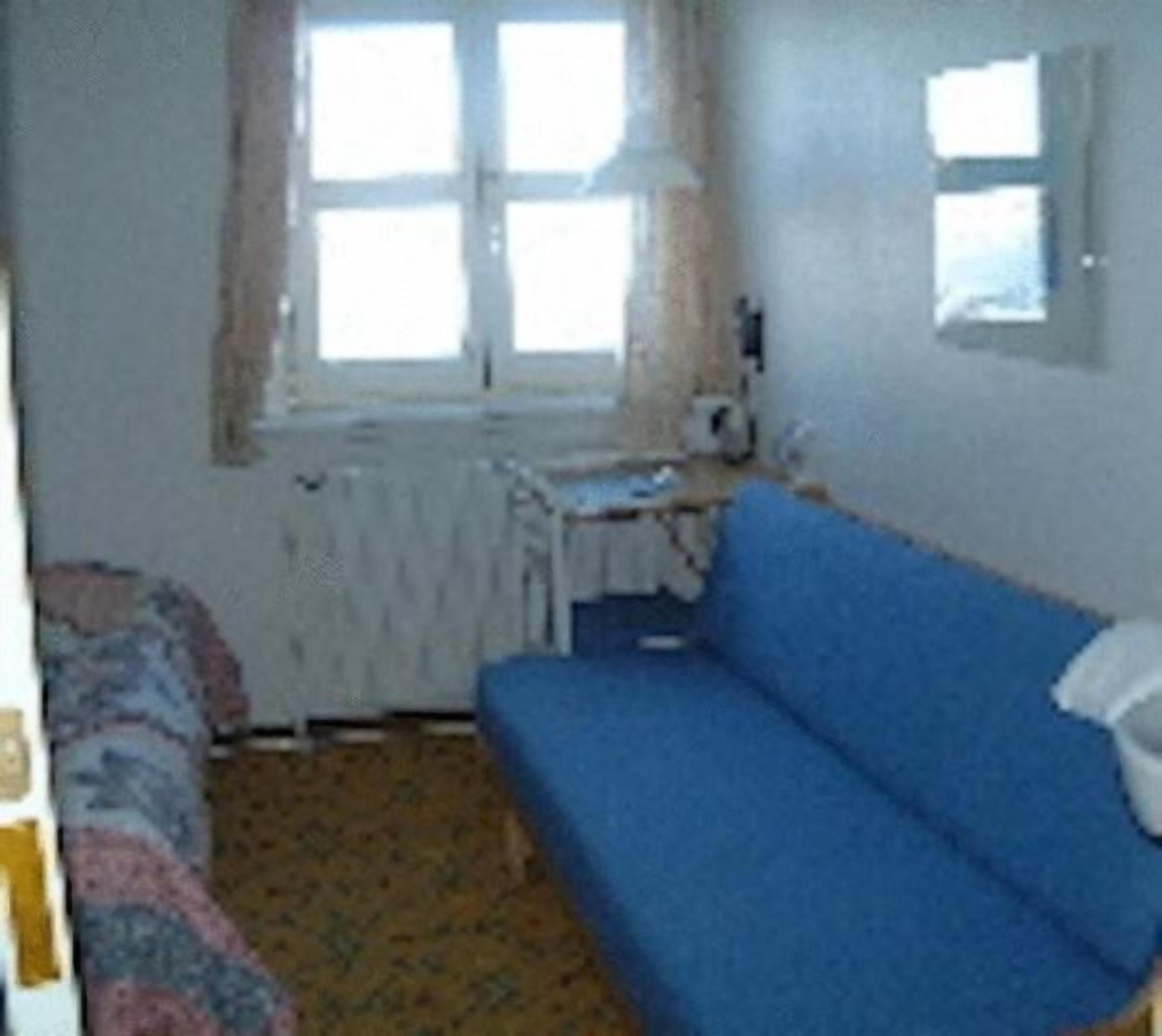 A small room with a blue sofa, a small table, a radiator, and a window with curtains.