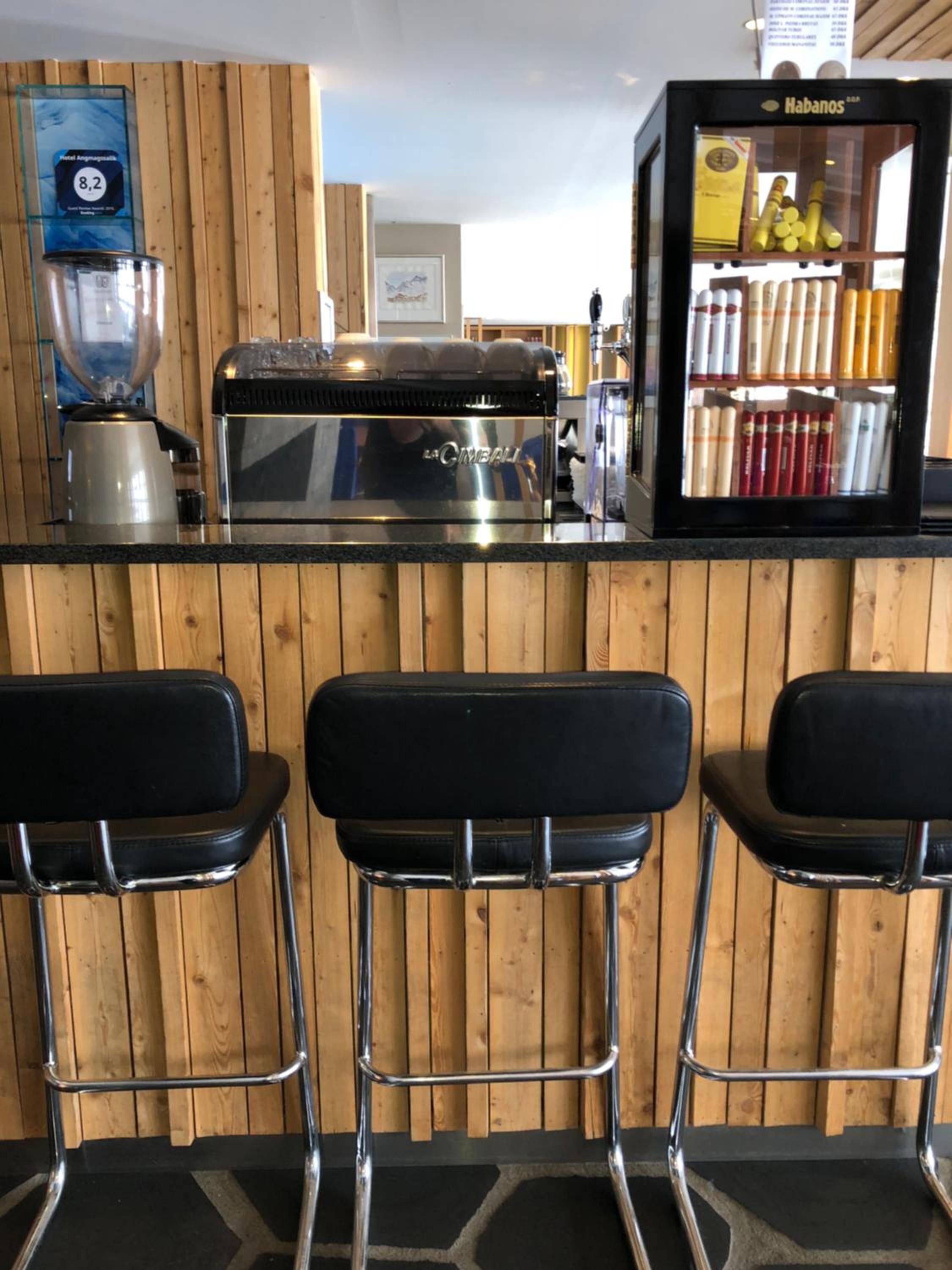 Een bar met een houten achtergrond, een koffieapparaat, een blender en een vitrine met flessen.