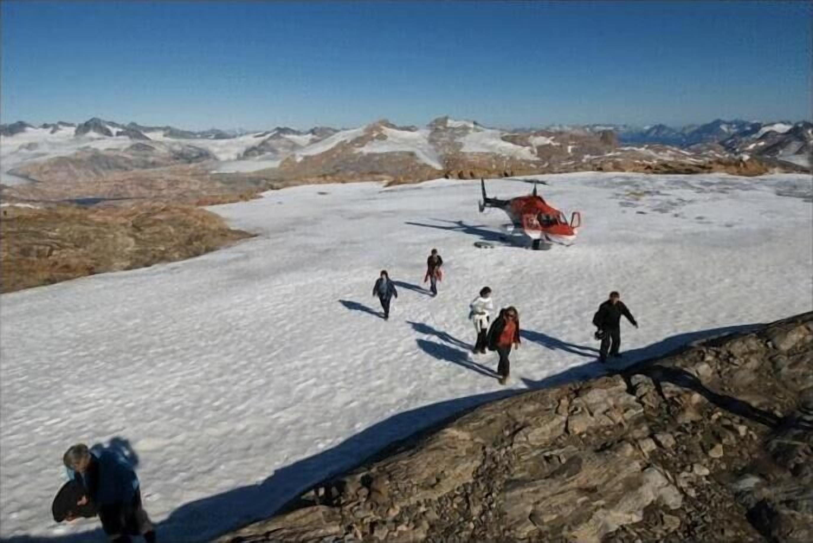 A group of people walking on a snowy mountain with a helicopter in the background.