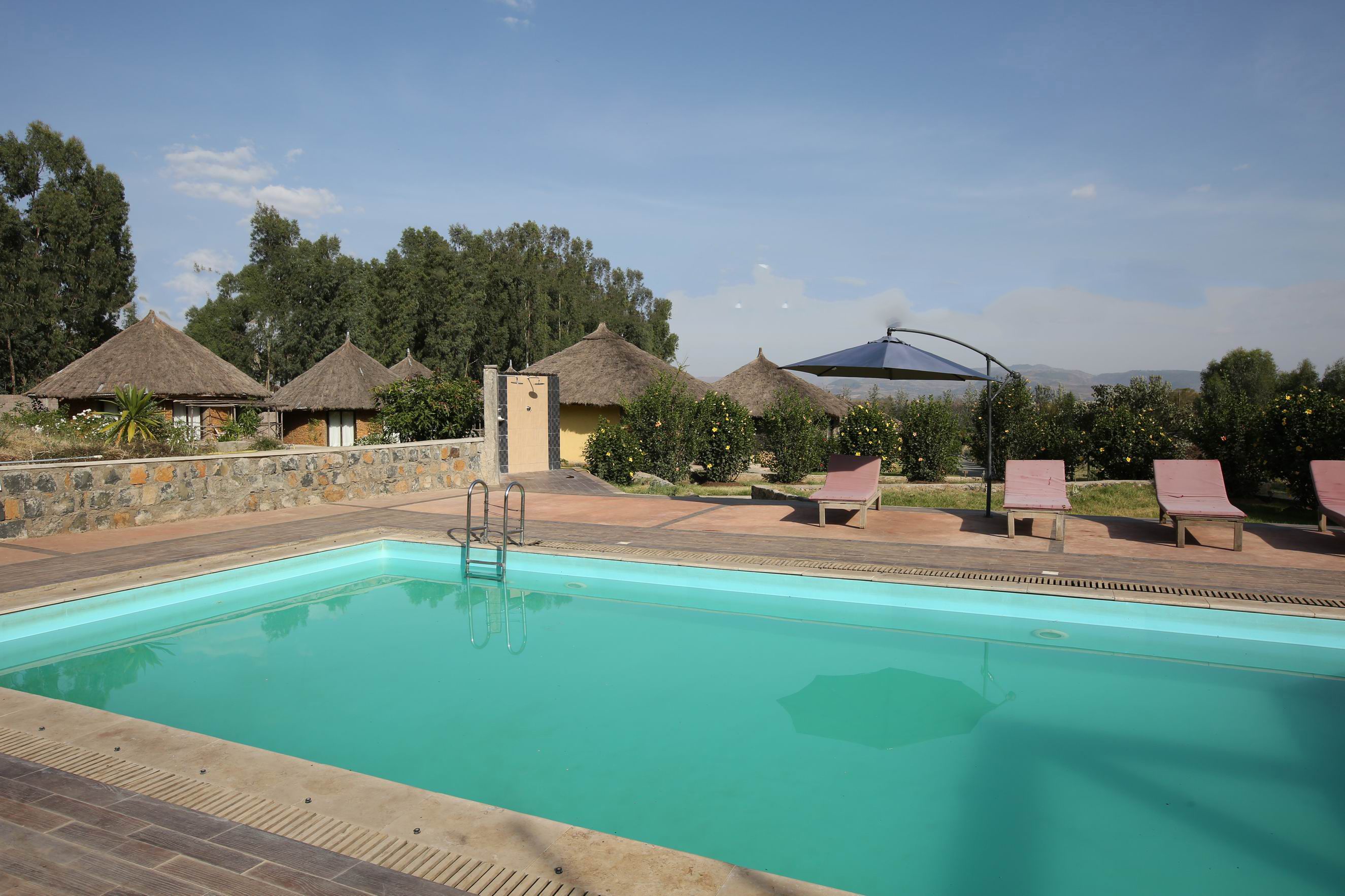 Una piscina con sillones de descanso y cabañas techadas de paja.