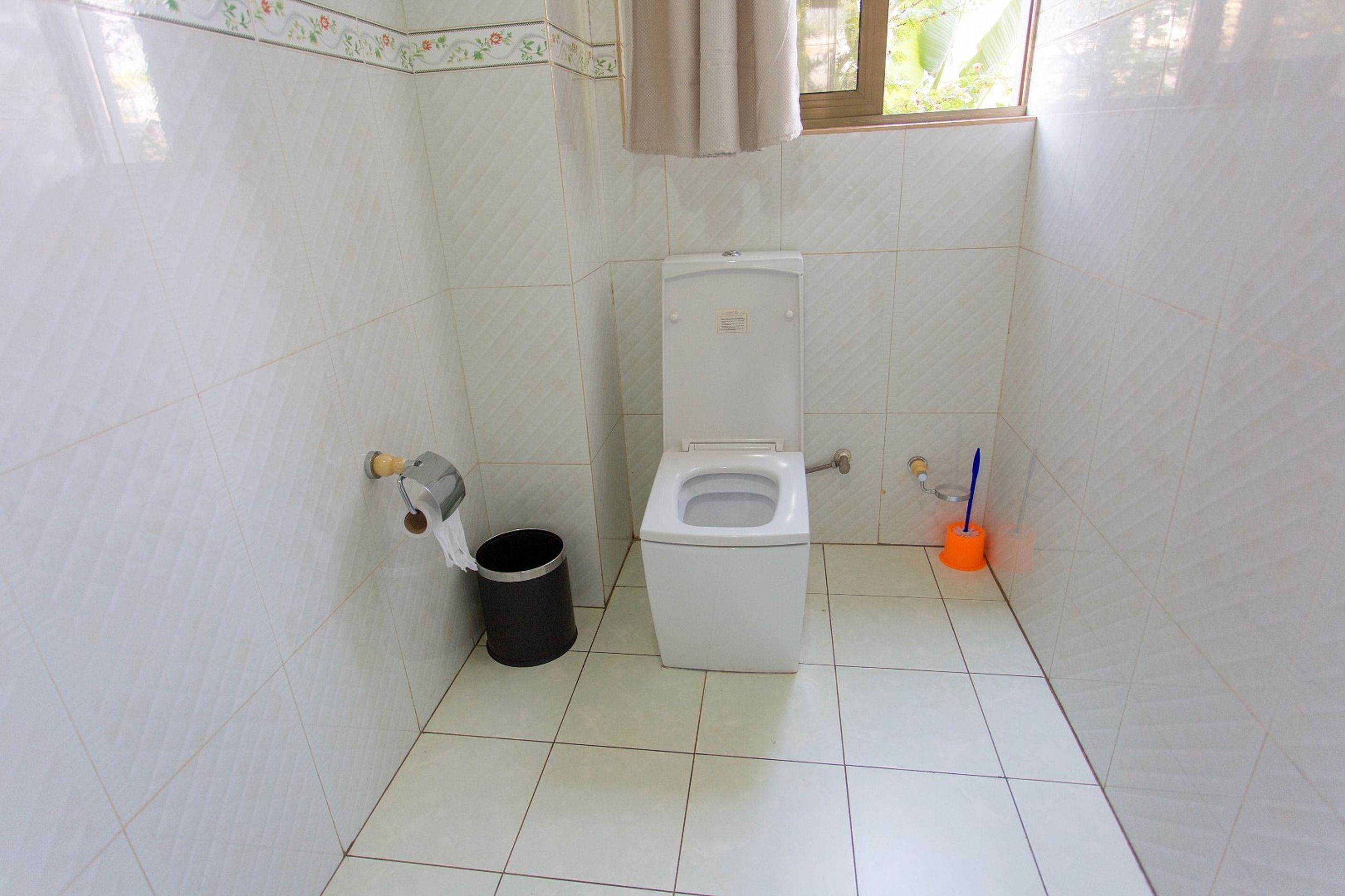 A small bathroom with a toilet, a trash can, and a window.