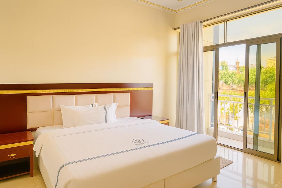 Une chambre d’hôtel avec un grand lit, une tête de lit en bois, une table de chevet et une vue sur l’extérieur grâce à une porte-fenêtre coulissante.