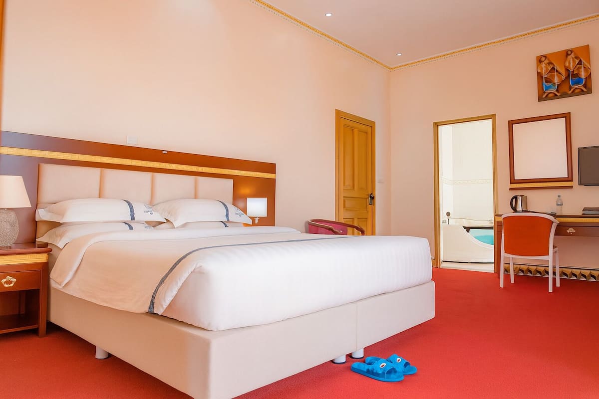 Une chambre d’hôtel avec un grand lit, un bureau avec une chaise, une télévision et une porte donnant sur une salle de bain.