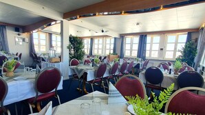 Un restaurant avec de nombreuses tables dressées pour le service, avec des chaises rouges et des nappes blanches.
