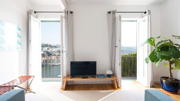 A modern living room with a large TV, a wooden bench, and a potted plant. - Arco Apartments (Porto)