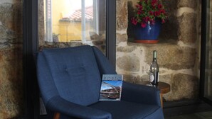 A room with a stone wall, a window, a chair, a small table with a bottle, and a potted plant. - Arco Apartments (Porto)