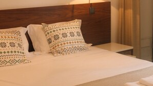 A neatly made bed with patterned pillows, a bedside lamp, and a view of a waterfall through a window. - Arco Apartments (Porto)