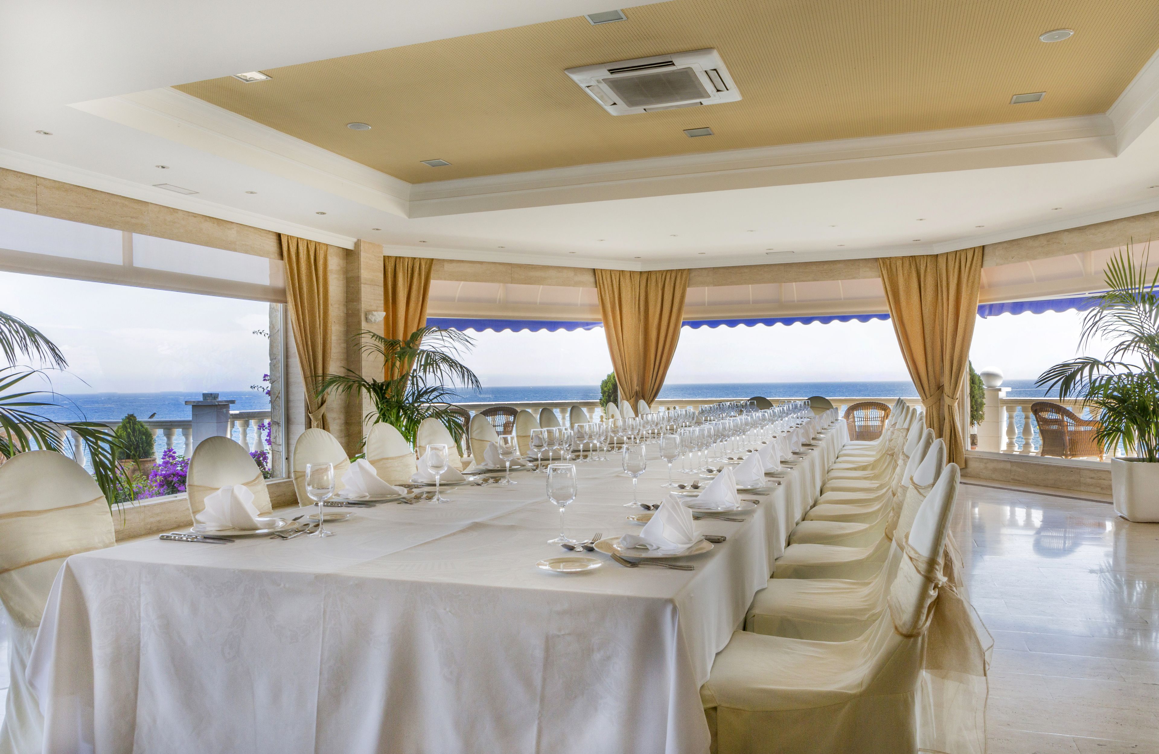 A long dining table set for a formal meal with a view of the ocean.