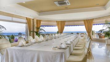 A long dining table set for a formal meal with a view of the ocean.