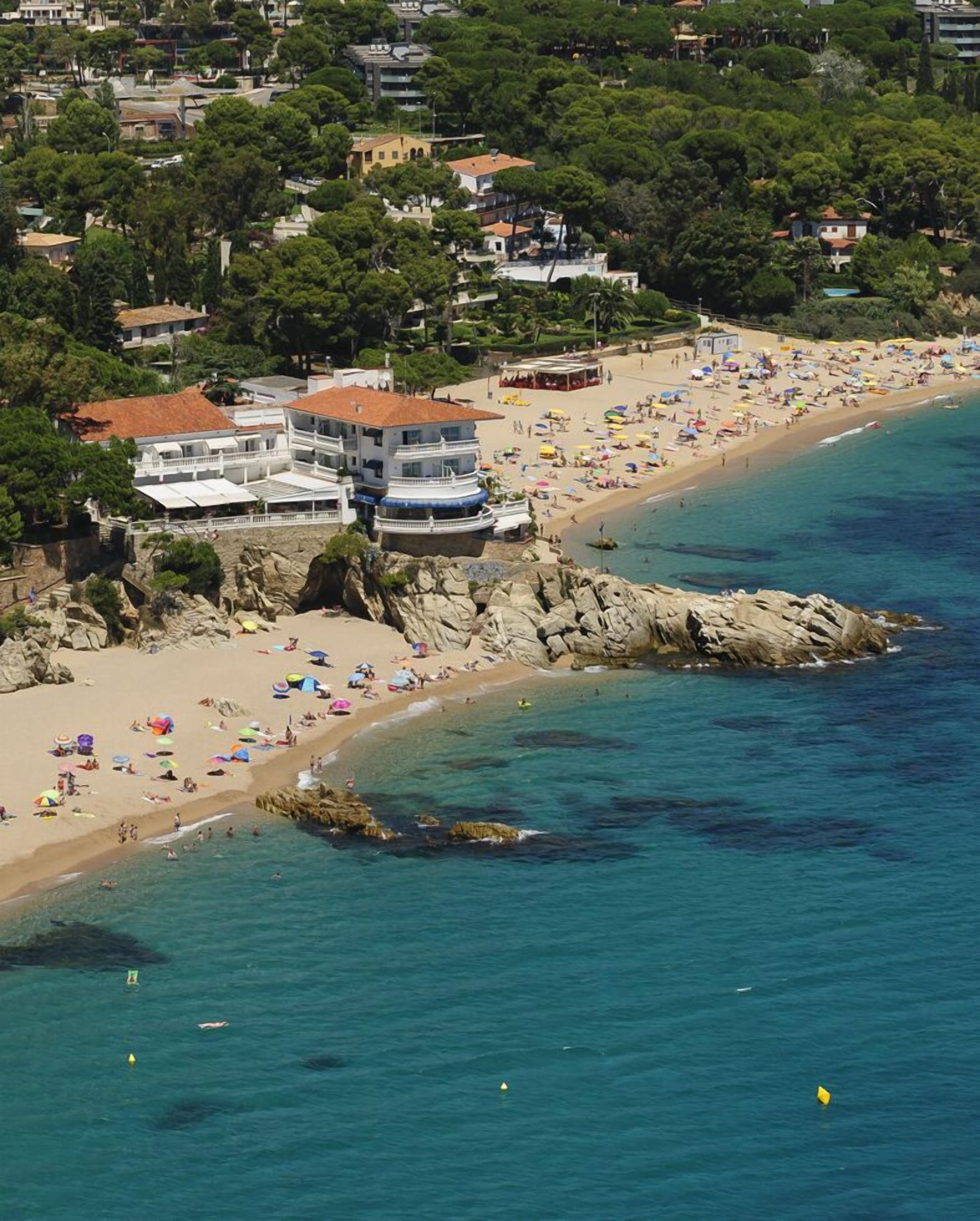 A coastal area with a beach, rocky shoreline, and buildings with balconies overlooking the sea.
