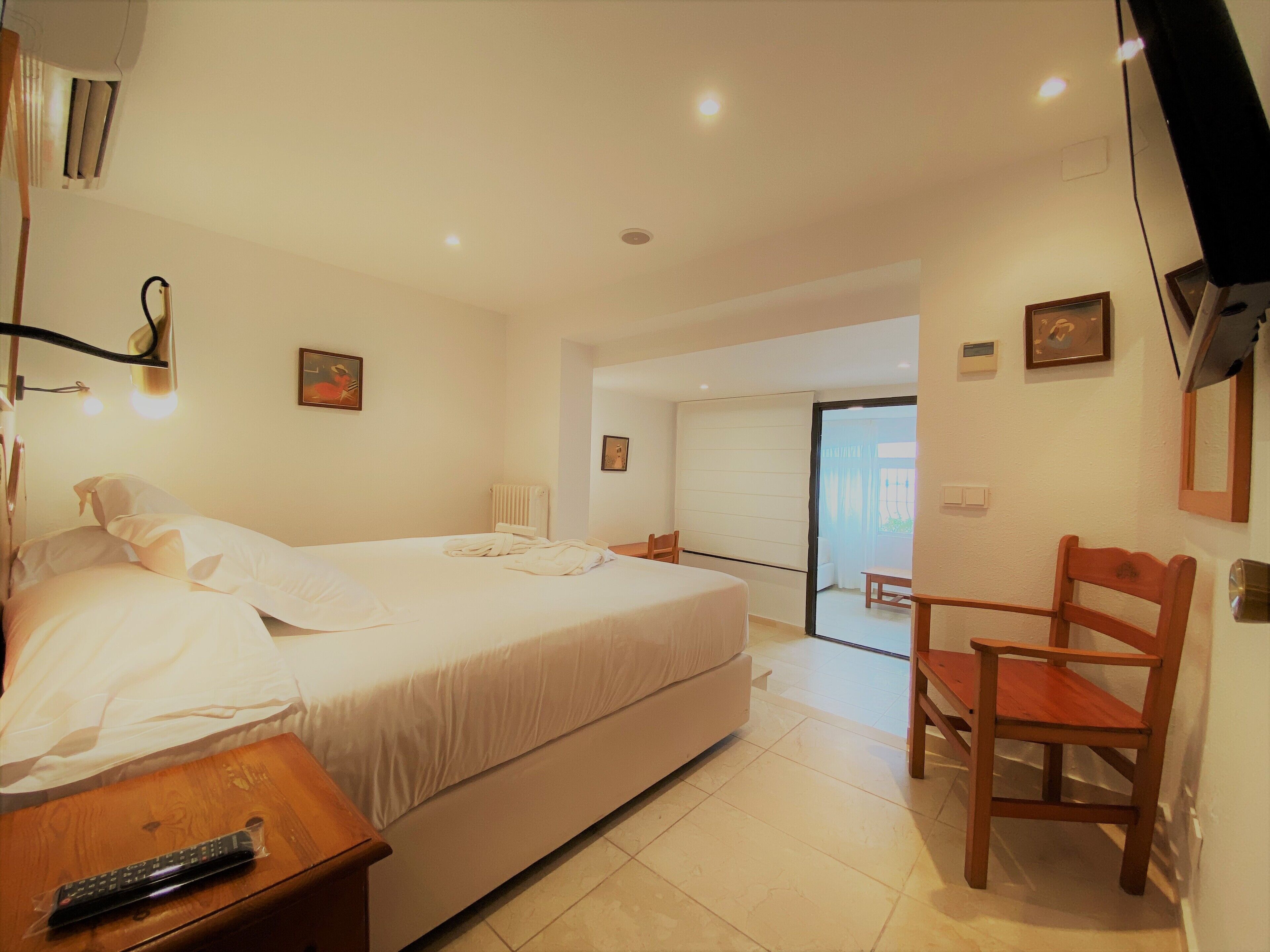 Habitación de hotel con una cama, una mesita de noche de madera, una silla y un baño visible a través de una puerta abierta.
