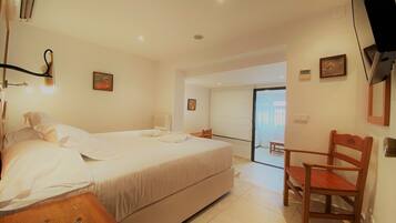 Habitación de hotel con una cama, una mesita de noche de madera, una silla y un baño visible a través de una puerta abierta.