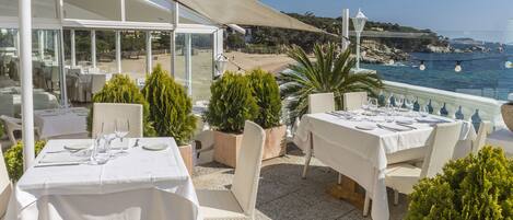 Un espace de restauration en plein air avec des tables disposées pour deux personnes, offrant une vue sur la plage et la mer.
