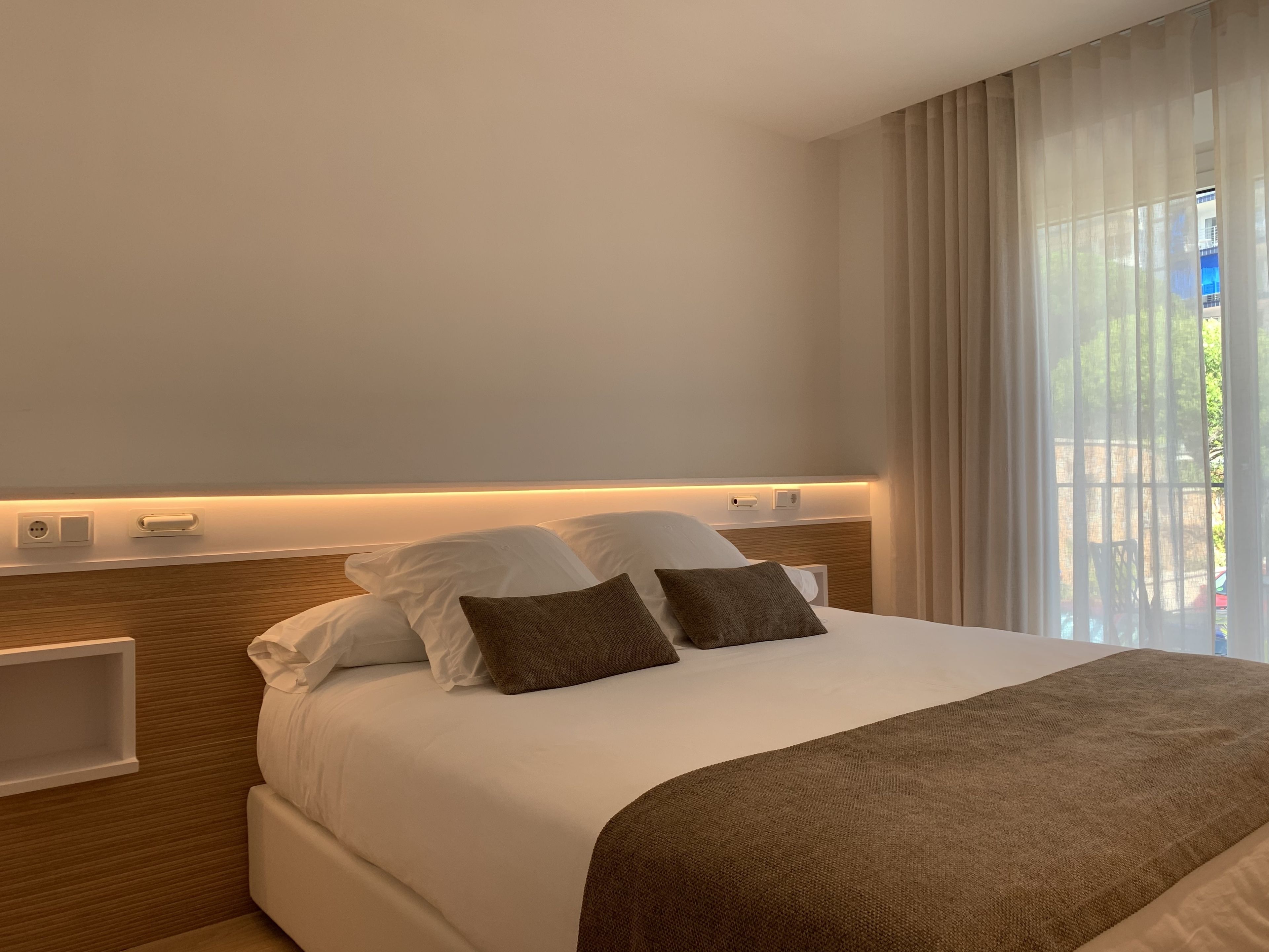 Una habitación de hotel con una cama bien hecha, una mesita de noche y vistas a zonas verdes.