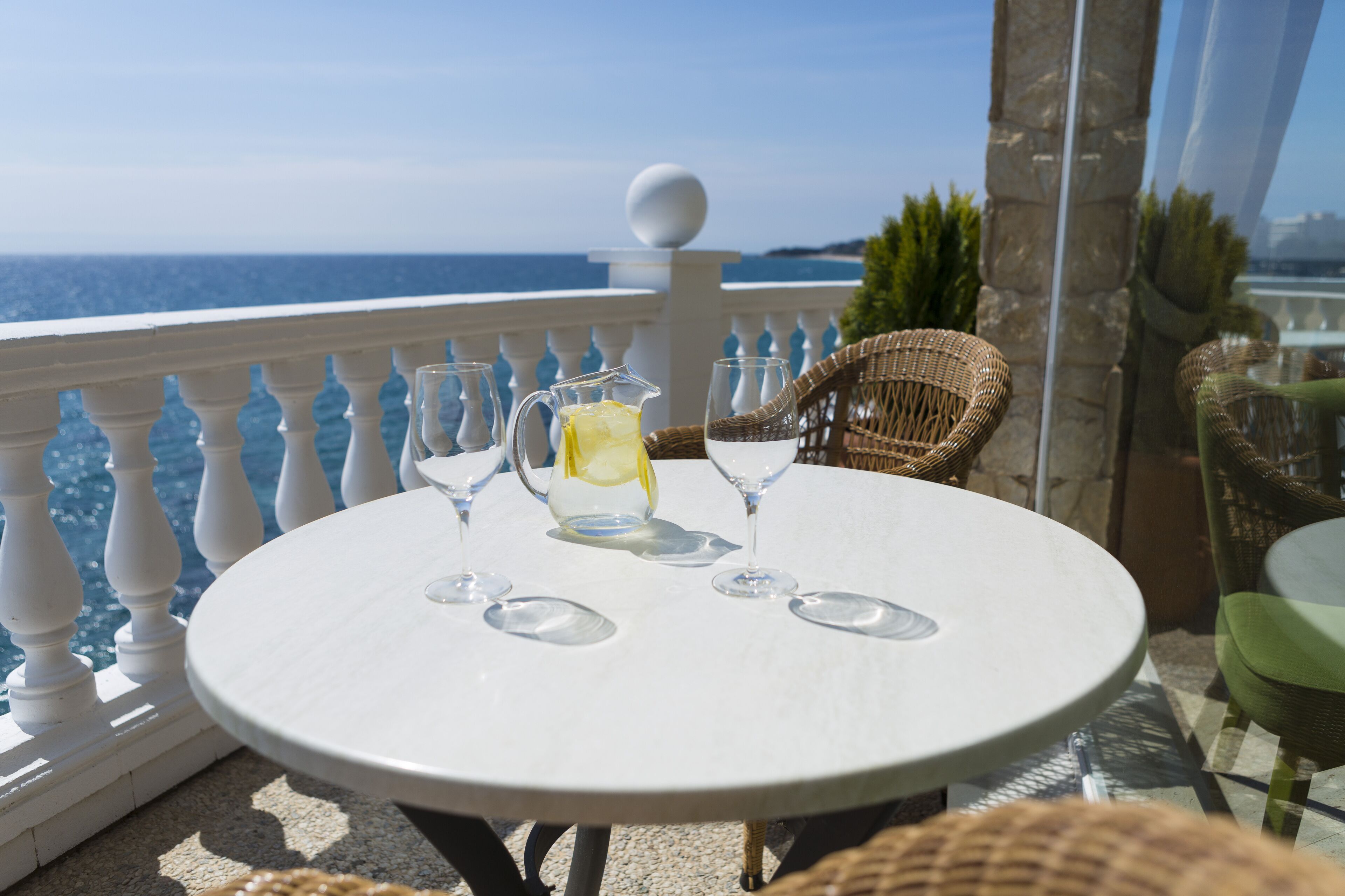 A round table with a pitcher and glasses on a balcony overlooking the sea.